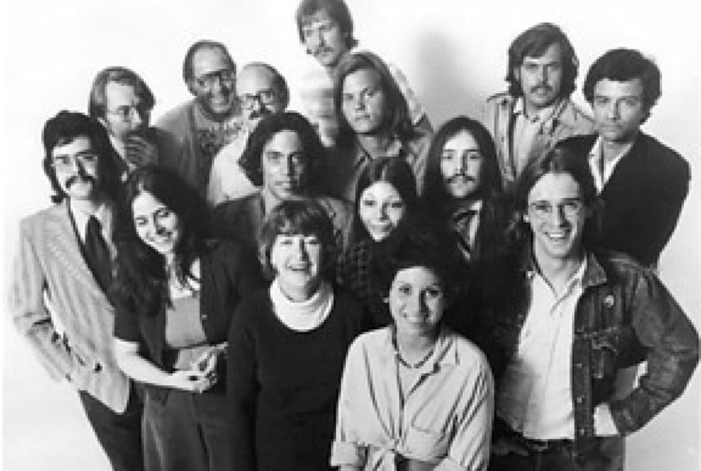 Black-and-white group portrait from the 1970s showing approximately 15 people—the early Chicago Poetry Center team—posed together in period clothing and hairstyles.