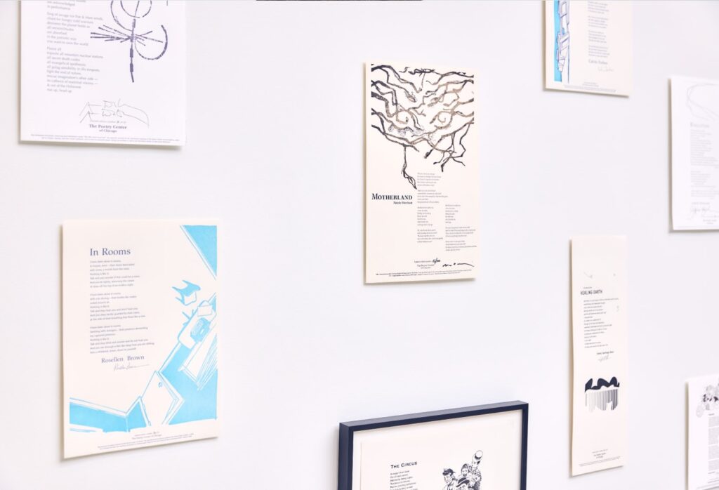 A gallery wall displaying poetry broadsheets featuring poems paired with original artwork, including pieces titled "In Rooms" by Rosellen Brown, "Motherland," and "The Circus."