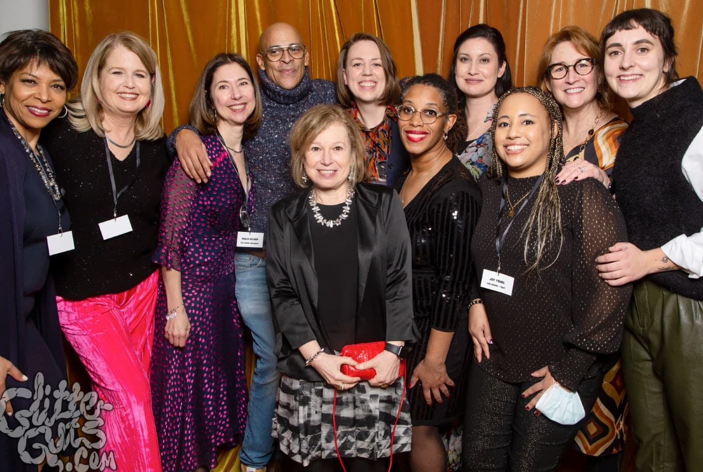 A group of about a dozen Chicago Poetry Center supporters pose together at a gala event, smiling in front of golden curtains, some wearing name tags.