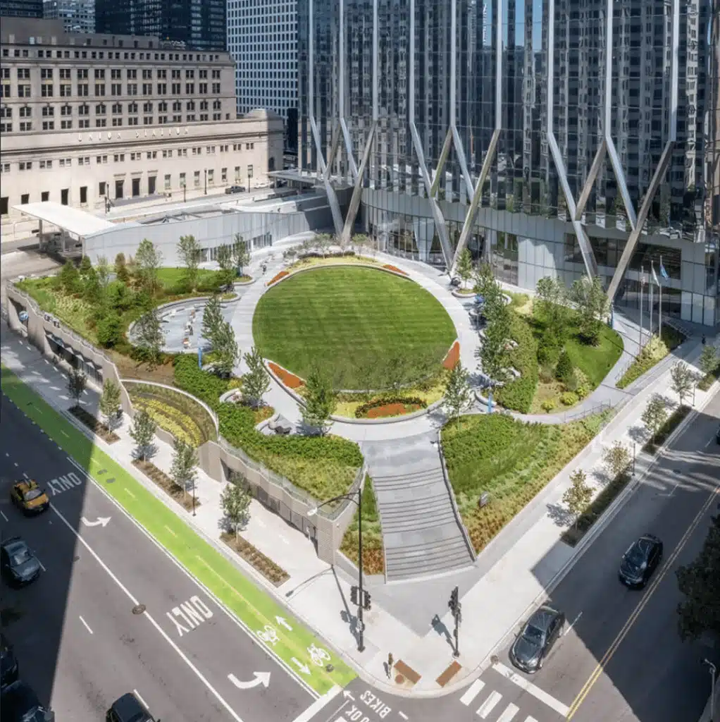 Aerial view of The Green at 320 South Canal, a landscaped urban park with a circular lawn, winding pathways, and terraced seating, nestled among downtown Chicago skyscrapers.